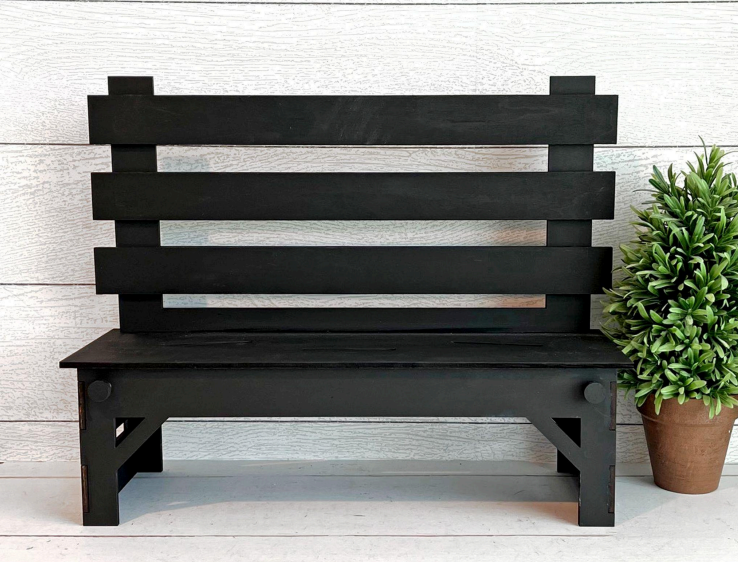 Black wooden bench against a light wooden paneled wall with a potted plant.
