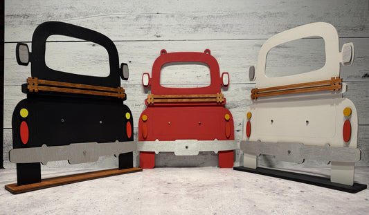 Three cardboard cutouts of cars in black, red, and white on a wooden floor.