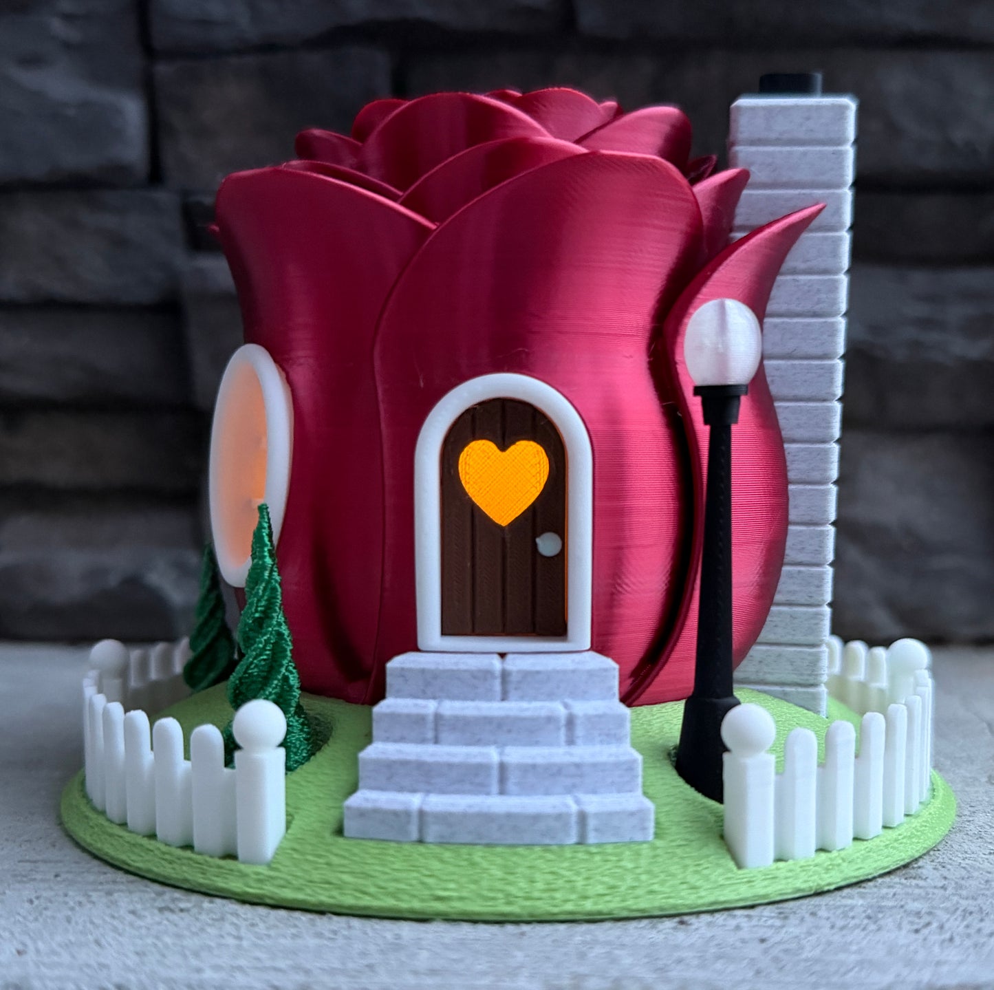 Model of a house with a heart-shaped door and a large red rose.