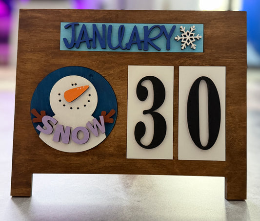 Wooden plaque with 'January 30' and snowman design on a blurred background