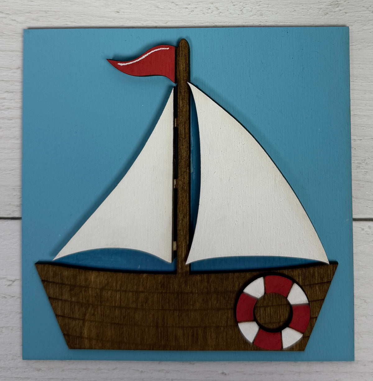 a wooden boat with white sails and a life preserver on a blue surface